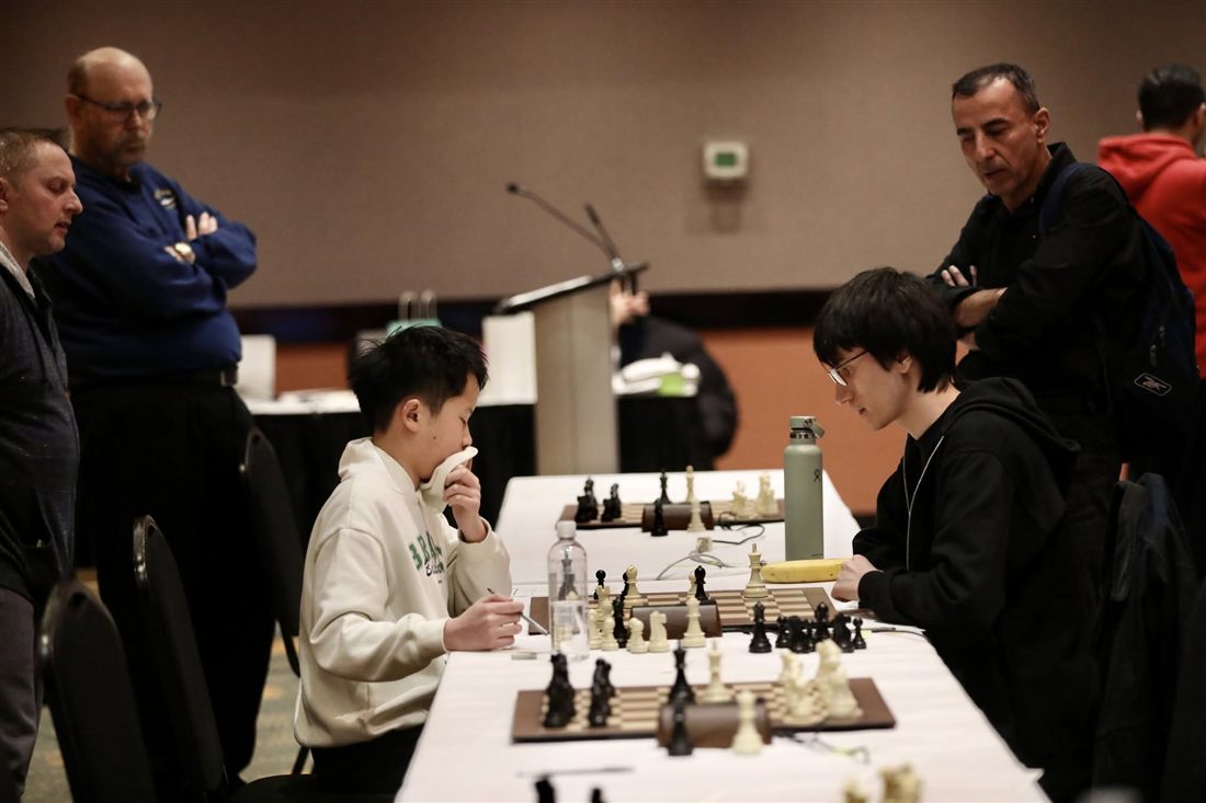 Two players deep in thought during a top-board game as arbiters look on